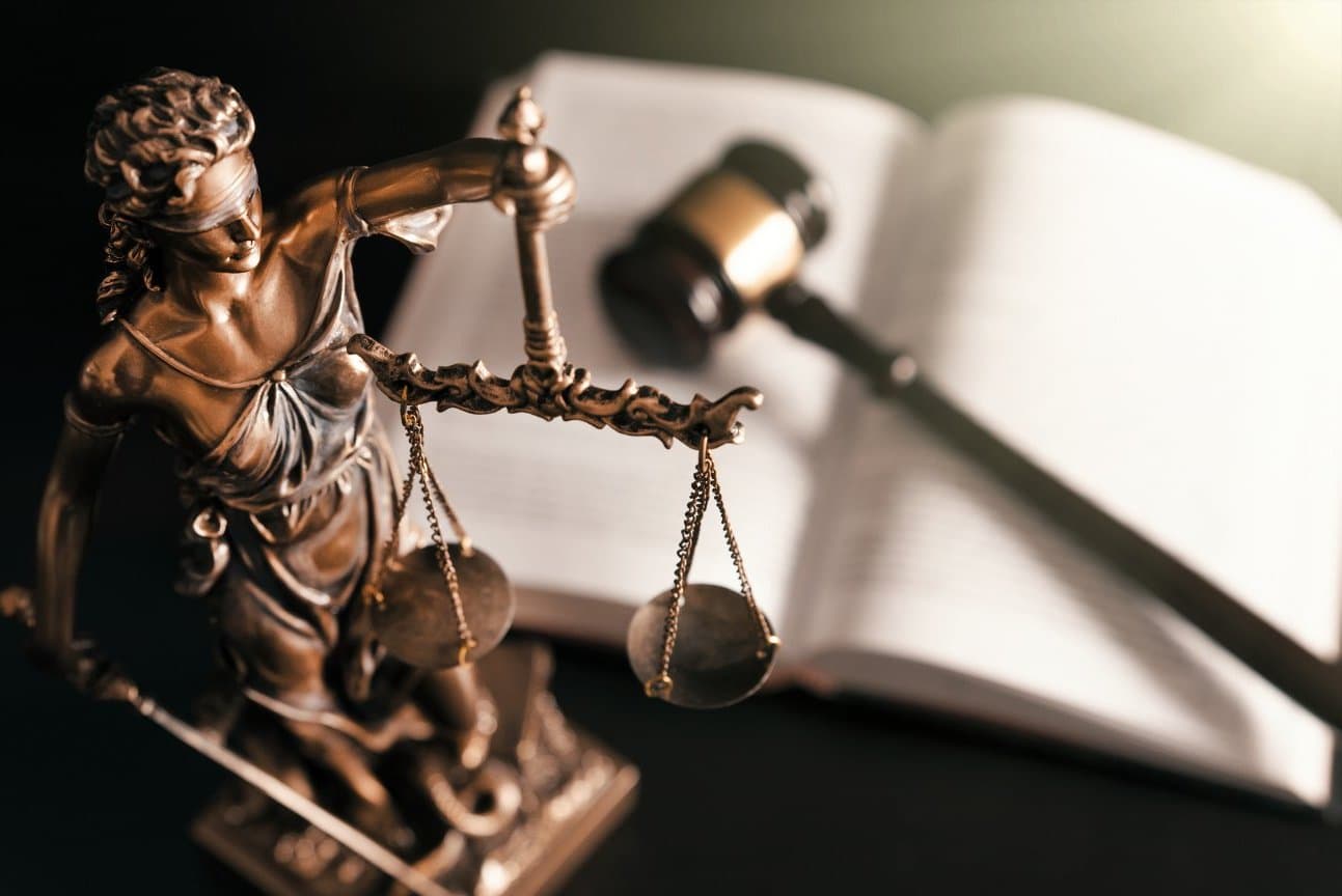 Bronze Lady Justice statue holding scales beside an open law book and gavel